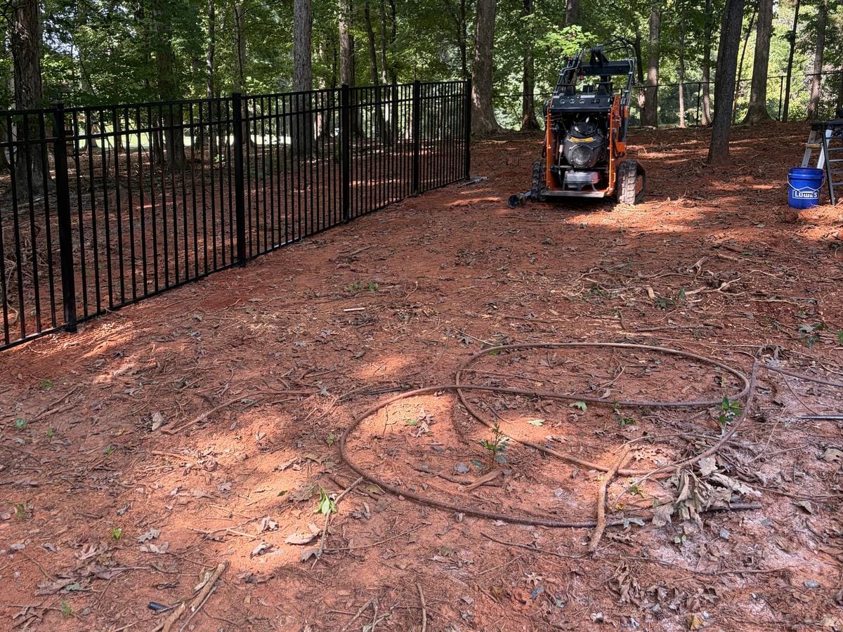 Black aluminum fence around a wooded back yard, with a compact track loader on site