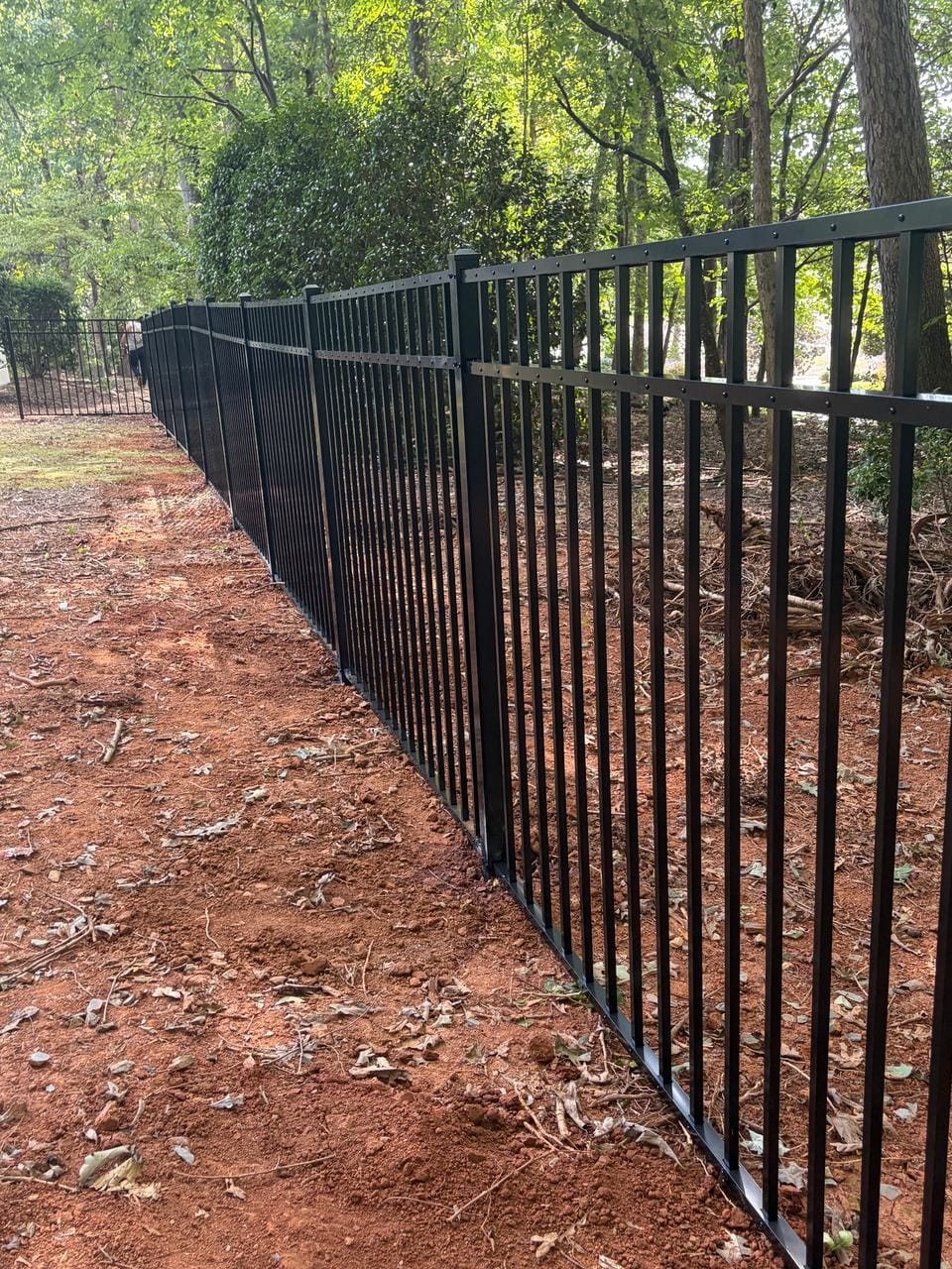 Long run of black aluminum fence through a wooded back yard