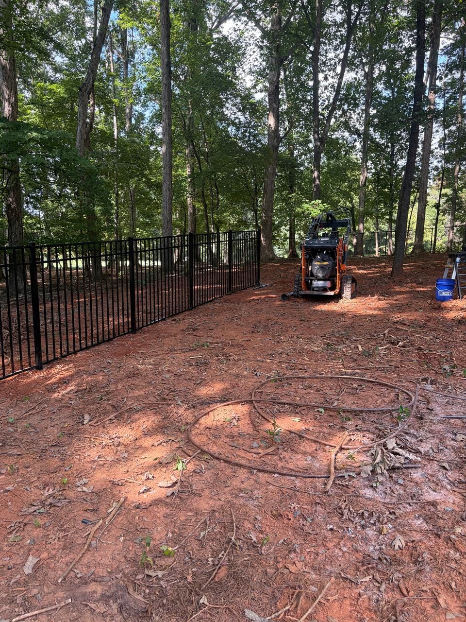 Black aluminum fence around a wooded back yard, with a compact track loader on site
