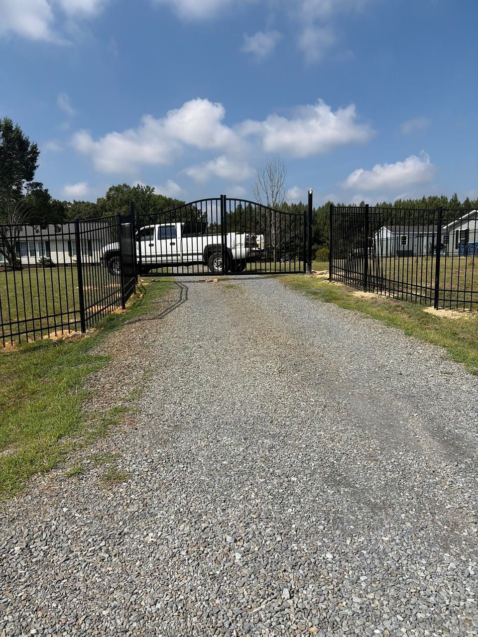 Black metal fence and arched double gate across a gravel driveway