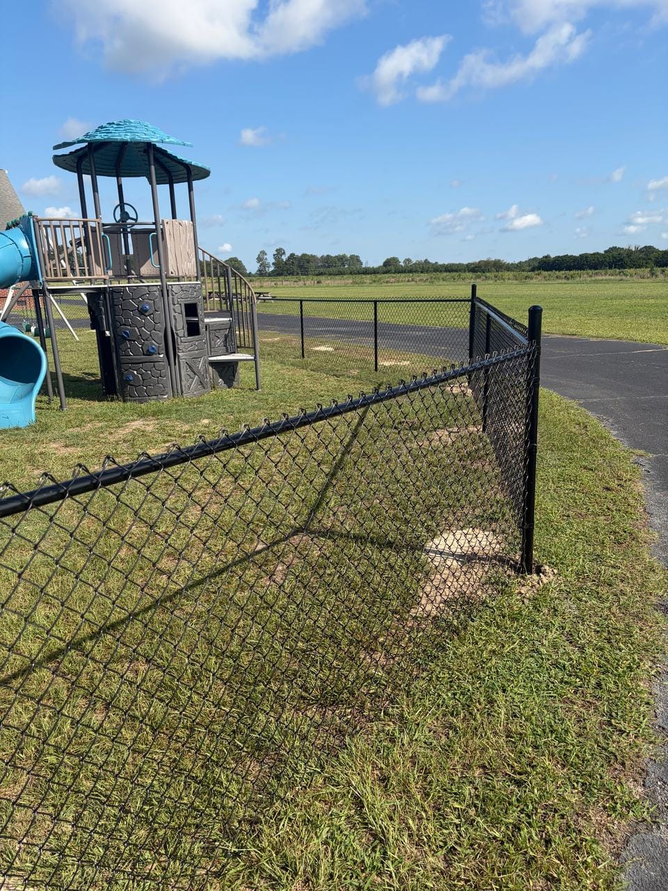 Black chain link fence corner beside a play set and a driveway