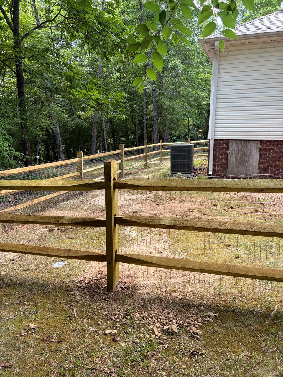 Wood post and rail fence with wire mesh behind a house
