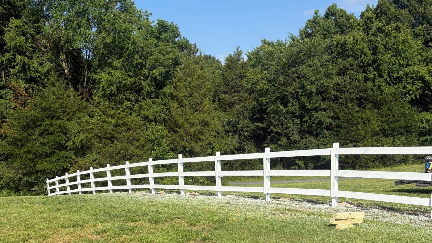 White vinyl three-rail ranch fence across a grassy slope