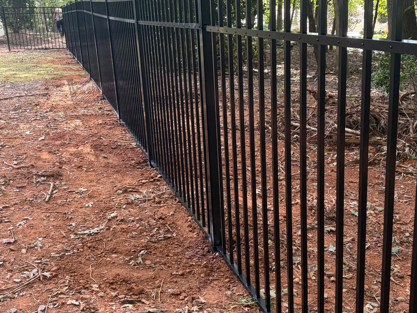 Long run of black aluminum fence through a wooded back yard